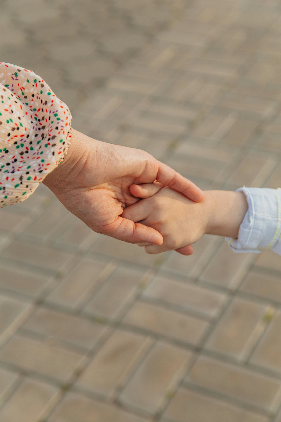 An adult hand gently holds a child's hand.